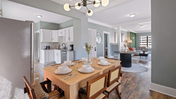 A modern kitchen with white cabinets, a wooden dining table set for four, and a chandelier.