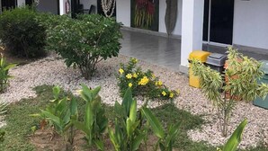 A covered outdoor area with a white building, a palm tree, and various plants. - Tuki Tuki Lodge, Tuki Tuki Lodge - Samara (Sámara)