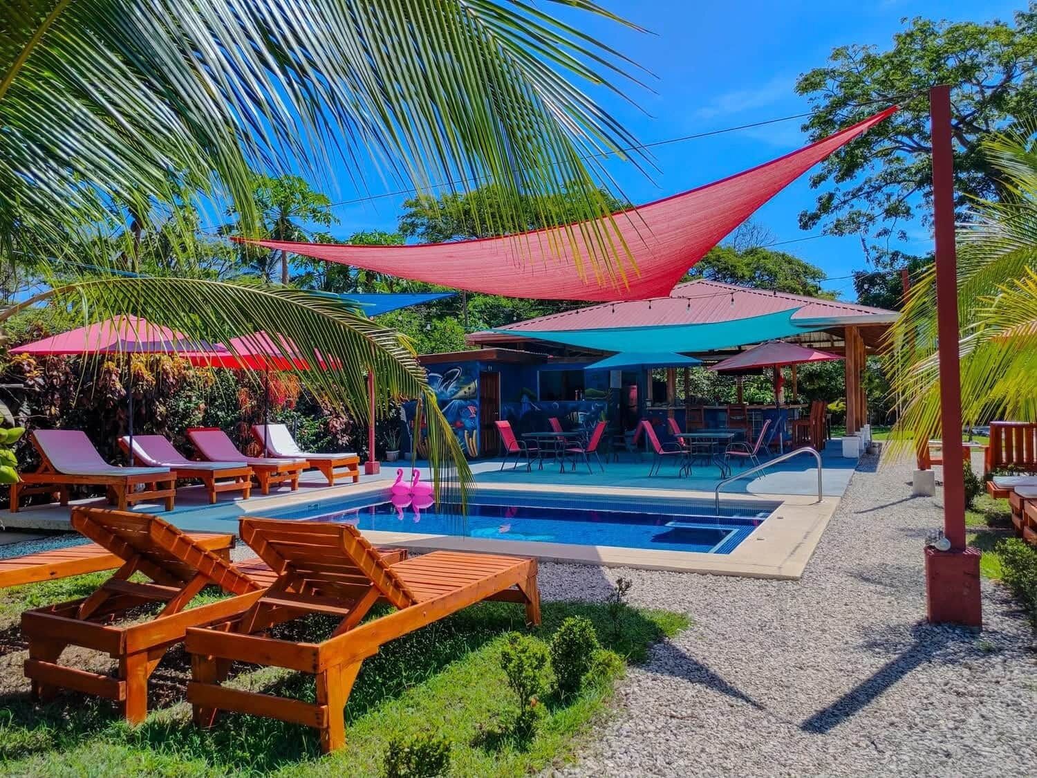 A pool area with lounge chairs and umbrellas, surrounded by greenery.