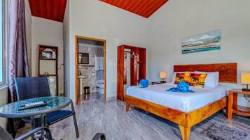 Una habitación de hotel con cama, una silla, una mesa, un baño y un cuadro en la pared.