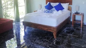 A hotel room with a large bed, a wooden headboard, a red armchair, and a painting on the wall. - Tuki Tuki Lodge, Tuki Tuki Lodge - Samara (Sámara)