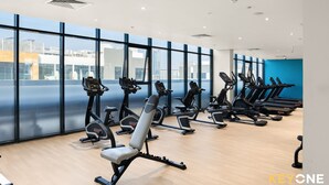 A modern gym with multiple treadmills and exercise bikes, large windows with a city view, and a wooden floor. - Azizi Riviera Studio with Chic Furnishing (Dubai)