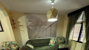 A living room with a green sofa, two patterned armchairs, a hanging light fixture, and a large wall mural. - Charming 2-bedroom townhome in welcoming Heredia with WiFi, AC in walkable town (Heredia)