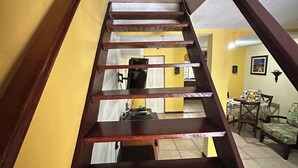 A wooden staircase with a handrail, leading to a room with yellow walls and a tiled floor. - Charming 2-bedroom townhome in welcoming Heredia with WiFi, AC in walkable town (Heredia)