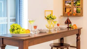 A dining area with a wooden table, two barstools, a vase with flowers, a fruit bowl, and a wall-mounted cabinet with a view.