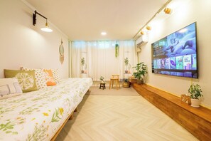 A bedroom with a bed, a TV, a desk, and potted plants.