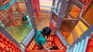 Un enfant joue sur un pont de corde à l’intérieur d’un espace de jeux équipé de structures en filet et de murs en verre.