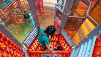 A child playing on a rope bridge inside a play area with netted structures and glass walls.