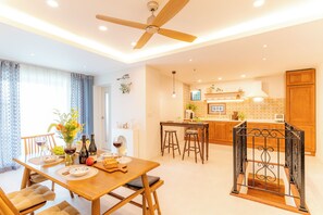 Une cuisine moderne avec des meubles en bois, un coin repas avec une table dressée pour deux personnes et un ventilateur de plafond.