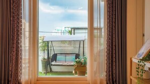 Une pièce dotée d’une grande fenêtre, d’un fauteuil suspendu à l’extérieur et de rideaux de chaque côté.