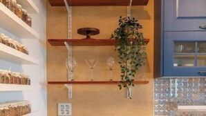 Une cuisine avec des meubles blancs, un four encastré, une plante suspendue et des étagères remplies de bocaux.