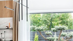 Ein moderner Essbereich mit einem Tisch für sechs Personen, Blick auf einen Baum und einer Wand aus Holzverkleidung.