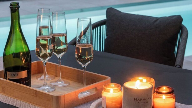 Ein Tisch, gedeckt mit einer Weinflasche, Gläsern und Kerzen, mit einem Pool im Hintergrund.