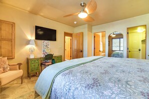 Ein Schlafzimmer mit einem großen Bett, einem Schreibtisch mit Lampe, einem Sessel und einem Fernseher an der Wand.