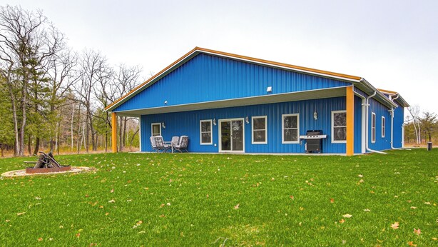 Een blauw huis met een grote tuin, een terras met stoelen en een barbecue.
