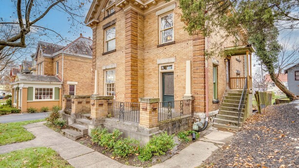 A traditional brick house with a front porch, a staircase leading to the entrance, and a small front yard with plants.