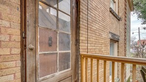 A wooden door with a glass panel, a brick wall, and a wooden railing.