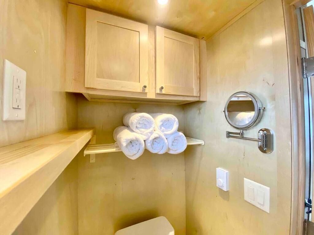 A small, compact bathroom with wooden cabinets, a toilet, and a towel rack with rolled towels.