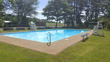 A rectangular swimming pool with a ladder and a lifeguard stand, surrounded by grass and trees.