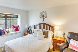 Relax in a serene bedroom with a large bed, comfortable armchair, and a view of lush greenery.