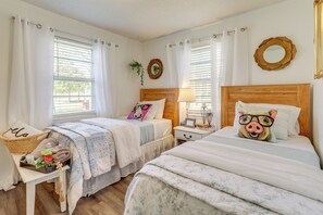 Une chambre avec deux lits, une table de chevet, une commode et une fenêtre avec des rideaux.