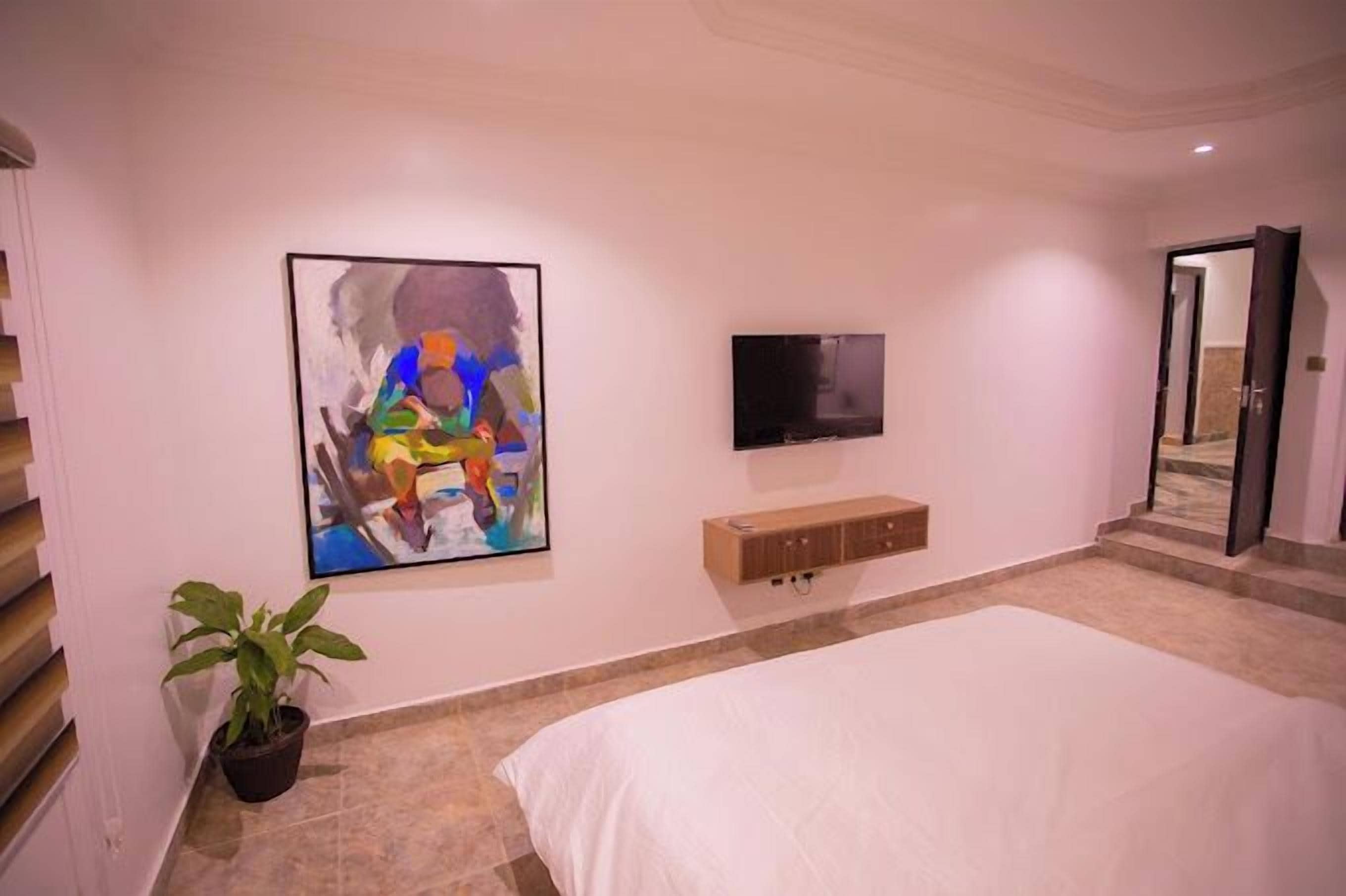 Een slaapkamer met een bed, een televisie, een schilderij, een plant en een houten kast.