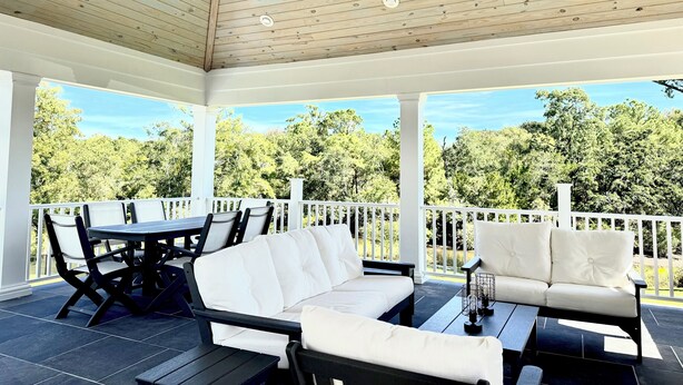 A covered patio with a wooden ceiling, white railings, and a view of a forest. - 3BR/3BA perfect location in Ocean Springs-walk to downtown-Moondance on Magnolia (Ocean Springs)