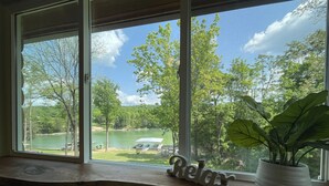 Une vue depuis une fenêtre donnant sur un lac, avec des arbres, un quai et une pancarte « Détendez-vous » posée sur le rebord de la fenêtre.
