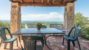 Un espacio de estar al aire libre cubierto, con una mesa, sillas, pilares de piedra y vistas al paisaje.
