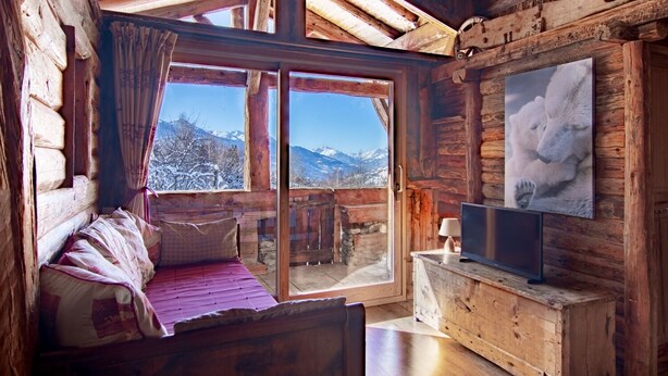 A cozy log cabin room with a bed, a television, and a large window offering a mountain view.