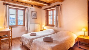 A cozy room with two beds, wooden furniture, and large windows.