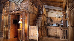 A rustic wooden cabin interior with a staircase, a small window, and a chandelier.