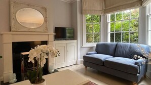 Un salon avec une cheminée, un téléviseur, un canapé et une fenêtre donnant sur un paysage verdoyant.