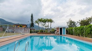 Una piscina con bordo in legno, circondata da una recinzione, e un piccolo edificio sullo sfondo.