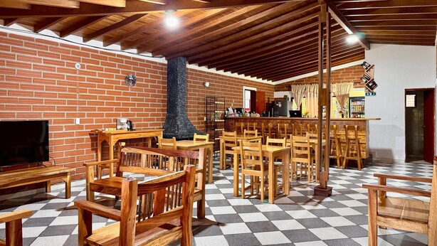Un'ampia stanza con panche e tavoli di legno, un muro in mattoni e un pavimento a scacchi.