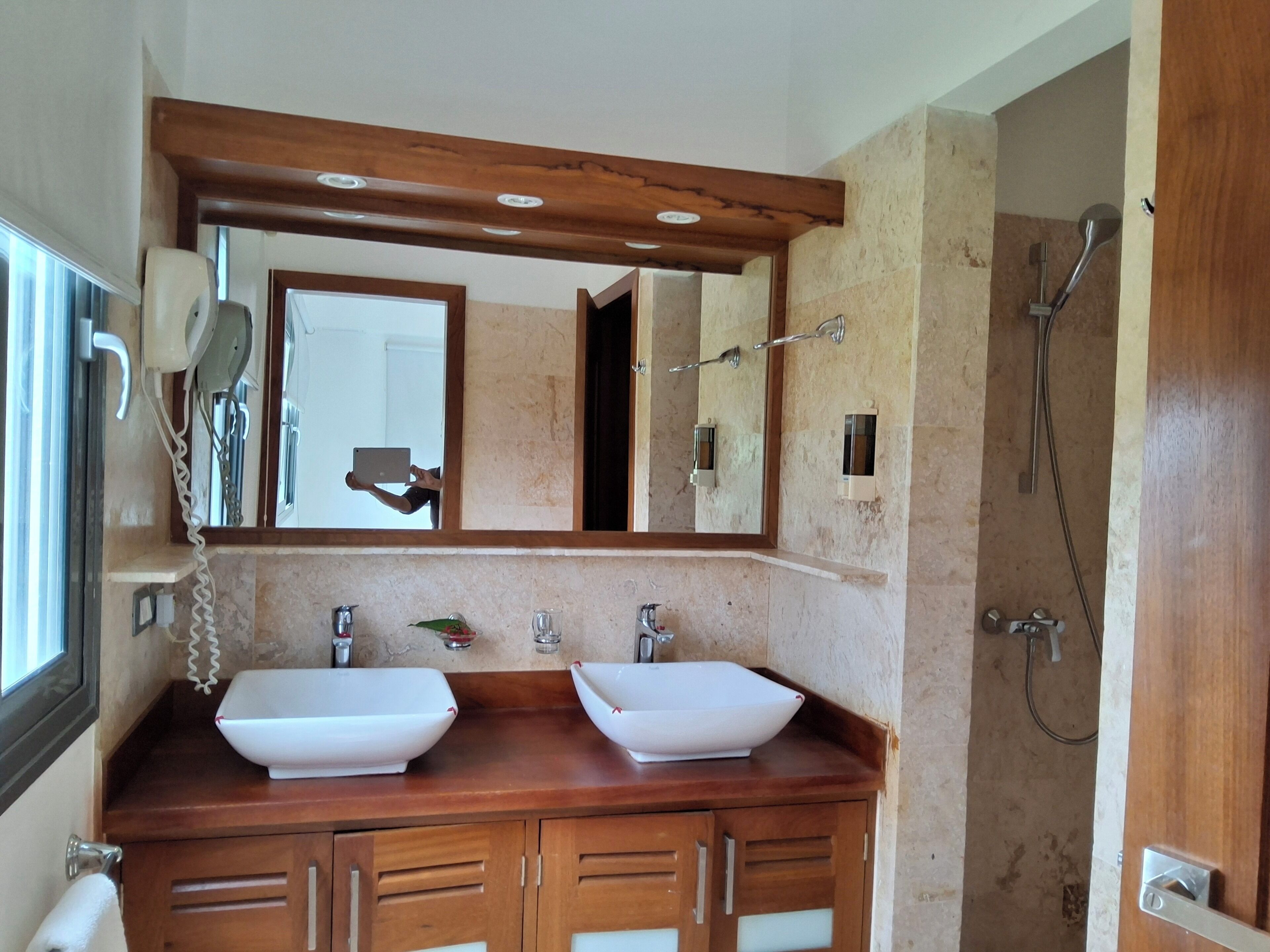 A bathroom with two sinks, a mirror, a shower, and wooden cabinetry.