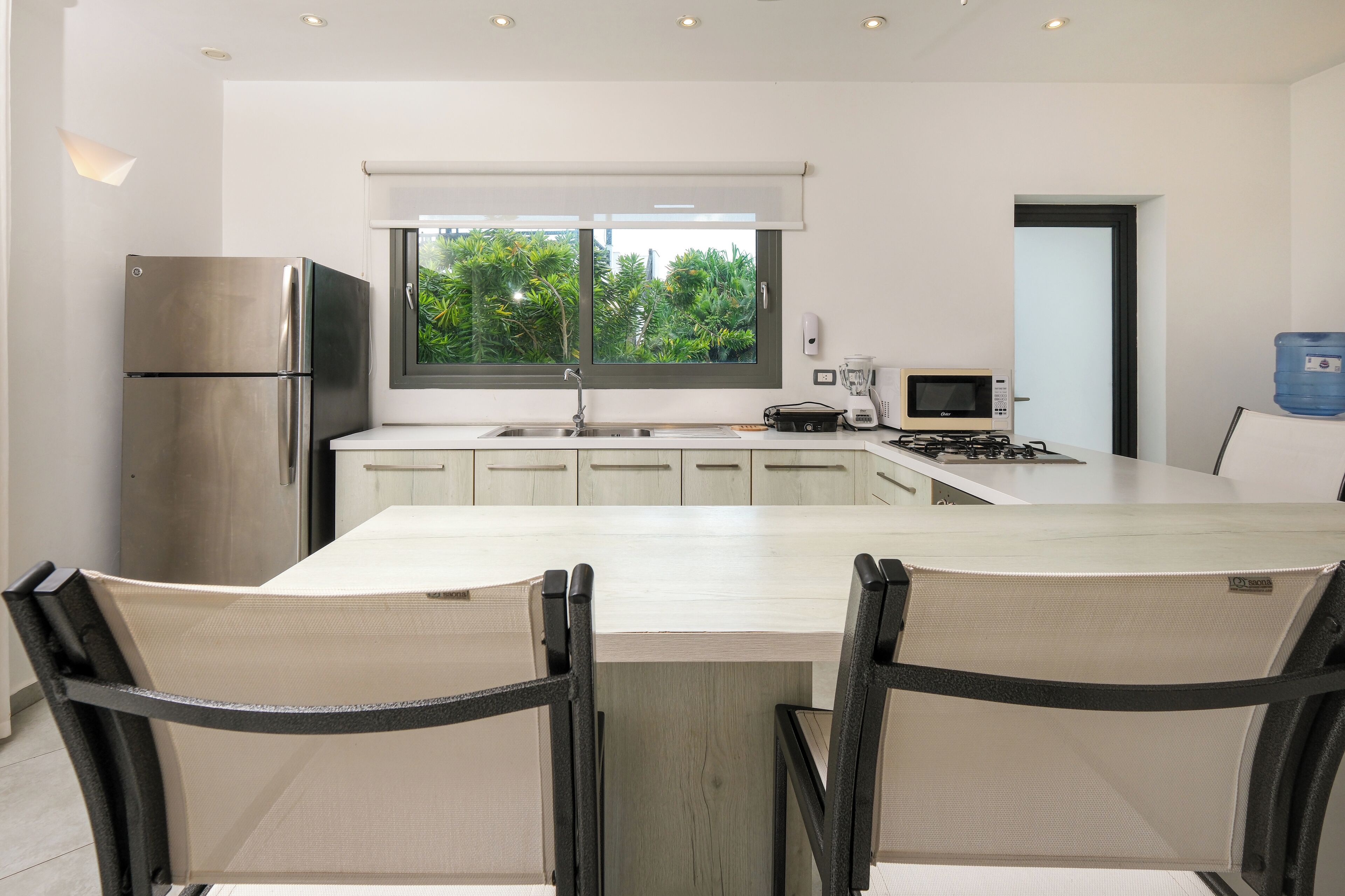 A modern kitchen with a large island, stainless steel appliances, and a view of greenery outside.