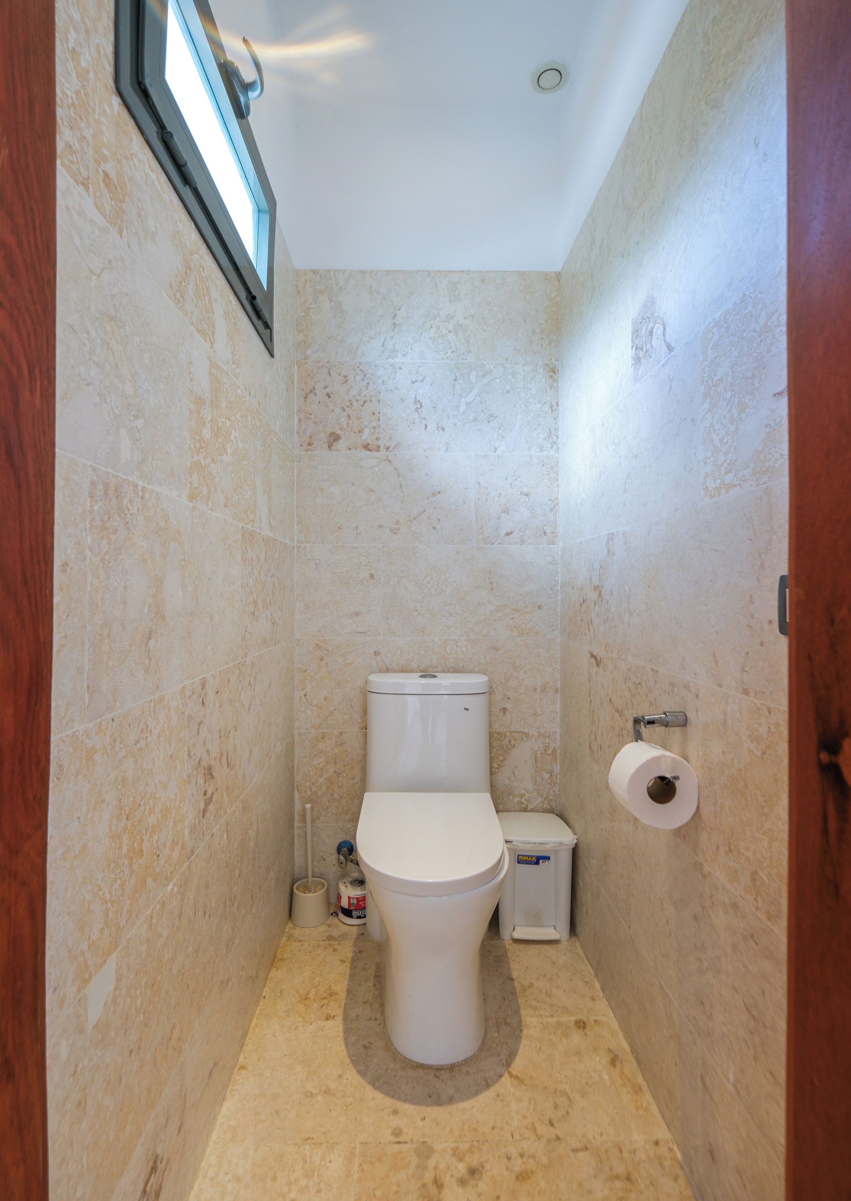 Um banheiro pequeno com azulejos, vaso sanitário, lixeira e rolo de papel higiênico na parede.