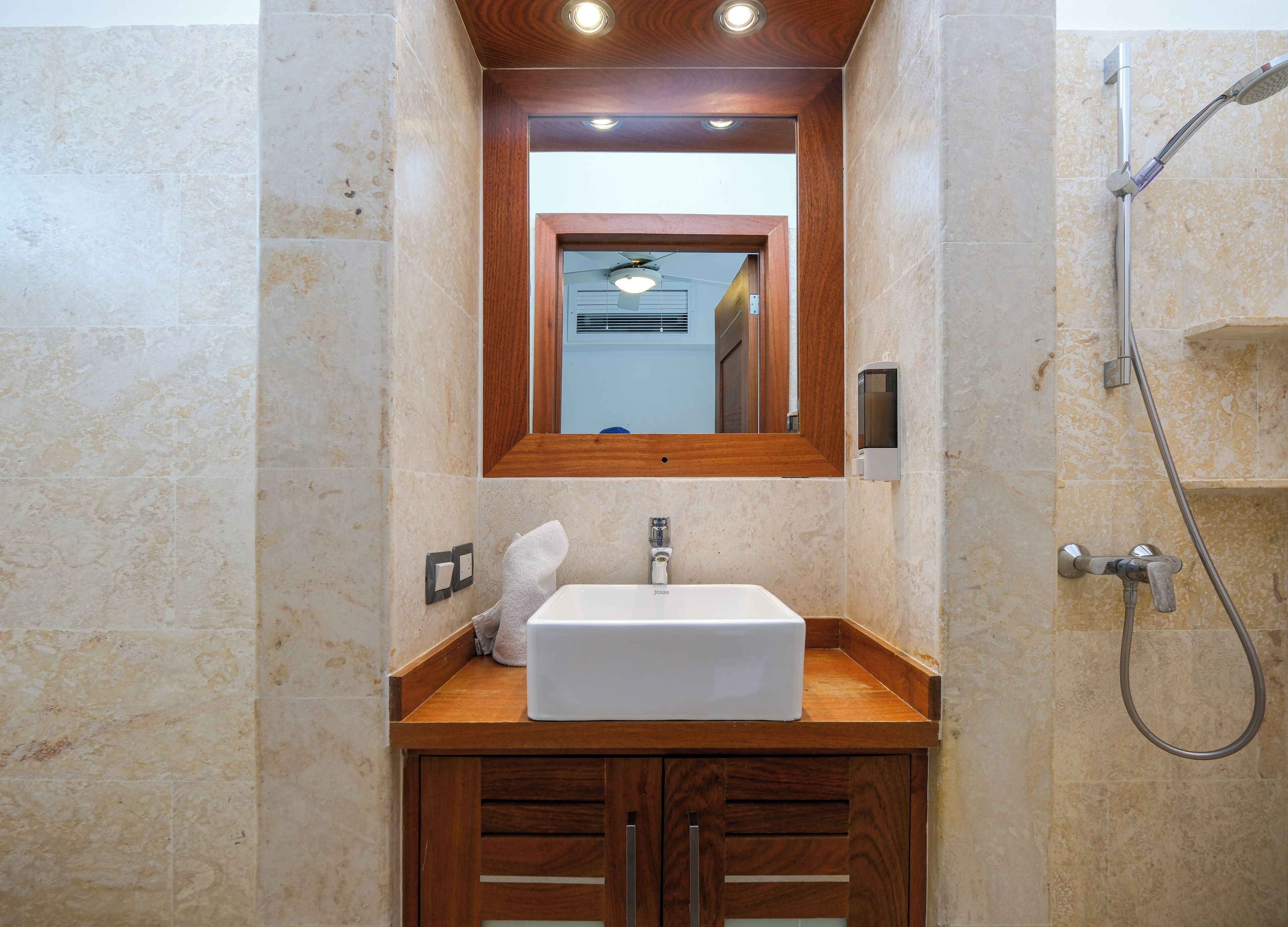 Un baño con lavabo blanco, tocador de madera, espejo y ducha.