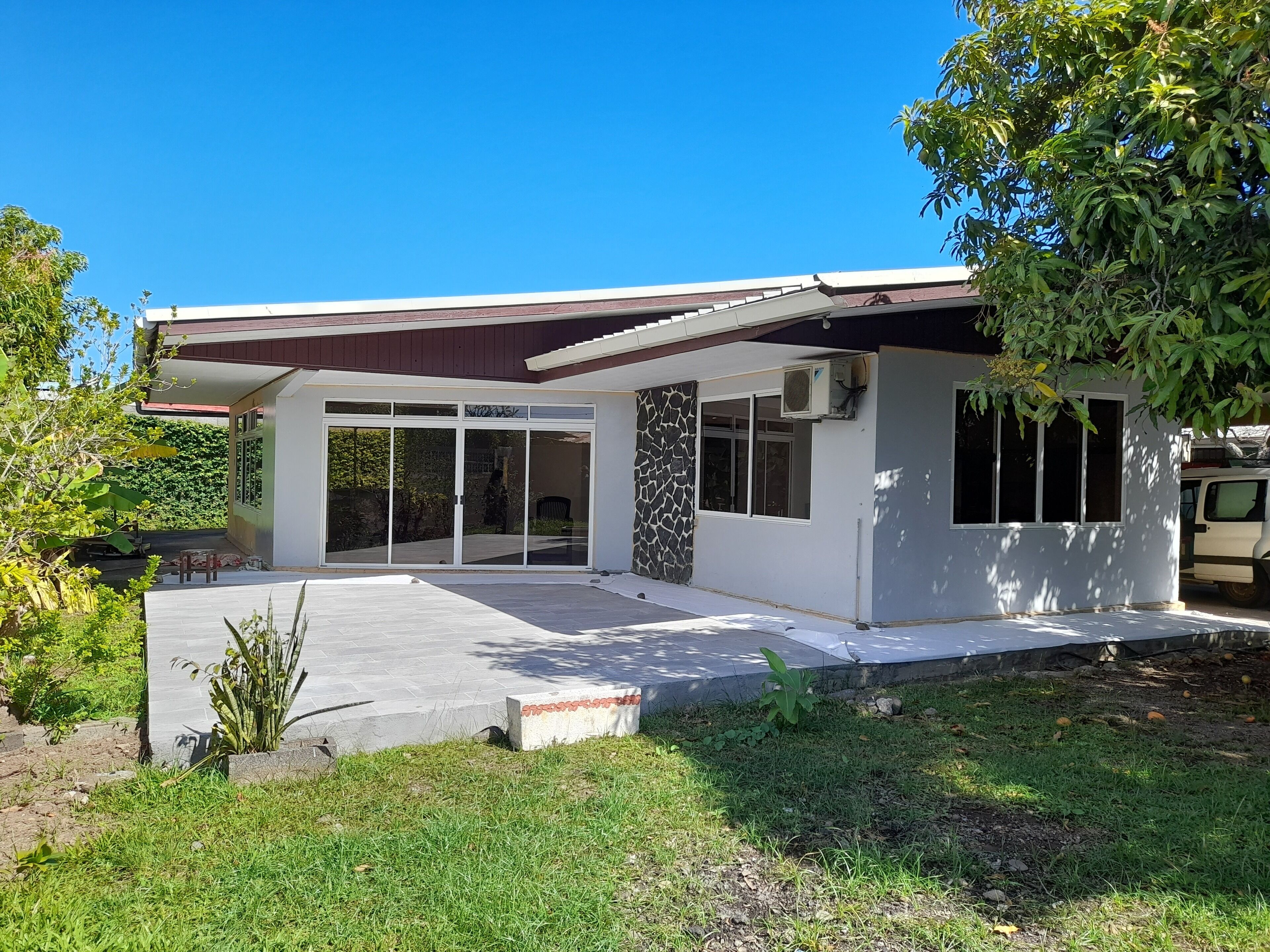 Une maison moderne dotée d’une grande entrée avec une porte-fenêtre coulissante, d’un mur décoratif en pierre et d’un patio couvert.