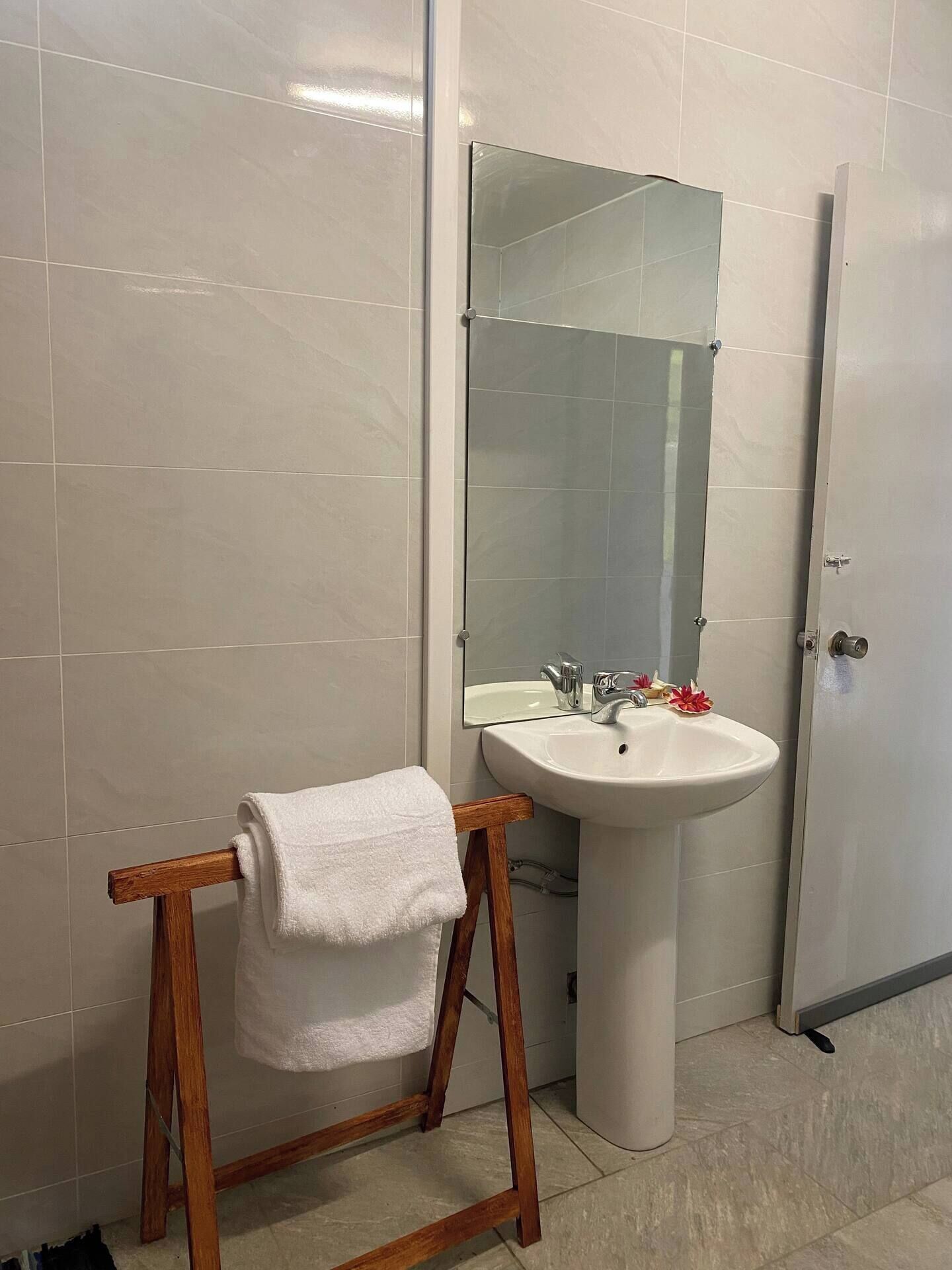 Een badkamer met een witte wastafel, een spiegel en een houten handdoekhouder.