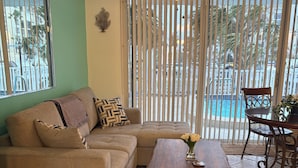 A living room with a sofa, a coffee table with flowers, a ceiling fan, and a view of a pool through large windows. - Charming and Spacious Studio in Delightful Clearwater Beach (Clearwater Beach)