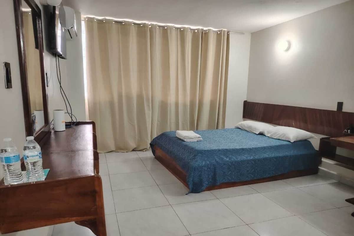A hotel room with a bed, a desk with water bottles, a TV, and a curtain.