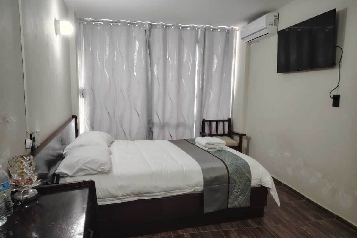 A bedroom with a bed, a bedside table, a chair, and an air conditioning unit on the wall.