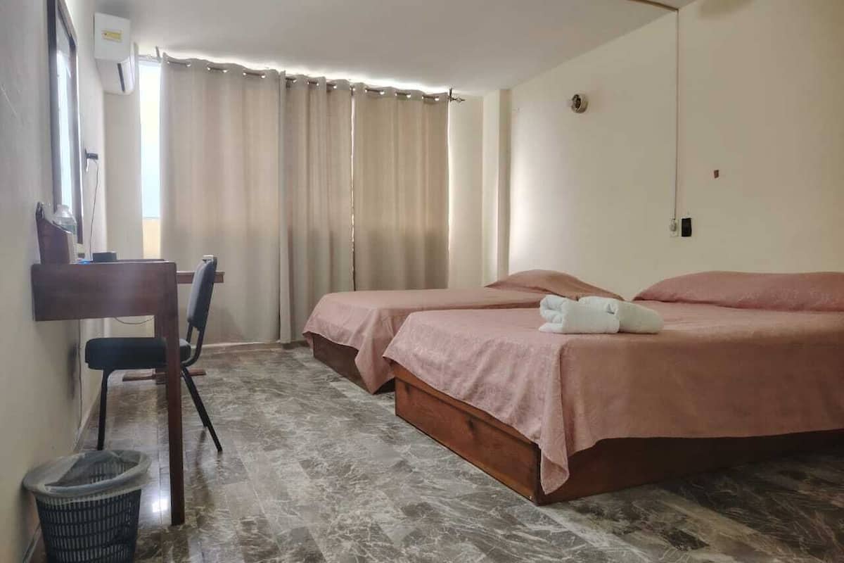 A hotel room with two beds, a desk, and a chair.