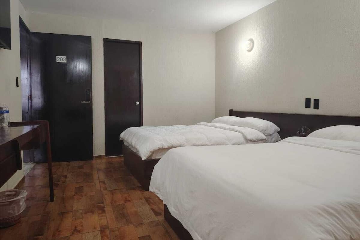 A hotel room with three beds, a desk, and a chair.