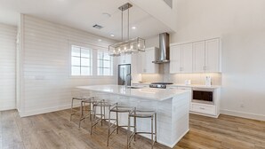 A modern kitchen with a large island, bar stools, stainless steel appliances, and white cabinetry.