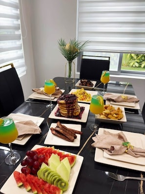 A dining table set with various dishes, including pancakes, fruit, and a small plant.
