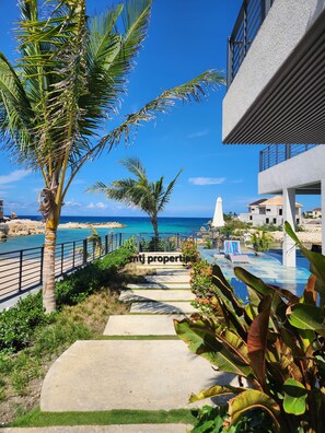 A pathway leading to a pool area with a view of the sea, surrounded by palm trees and a modern building. - The Onyx Beach Villa by MTJ Properties (Plantation Village)