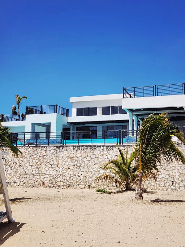 A modern multi-story building with a stone facade, a balcony with a black railing, and a clear blue sky.